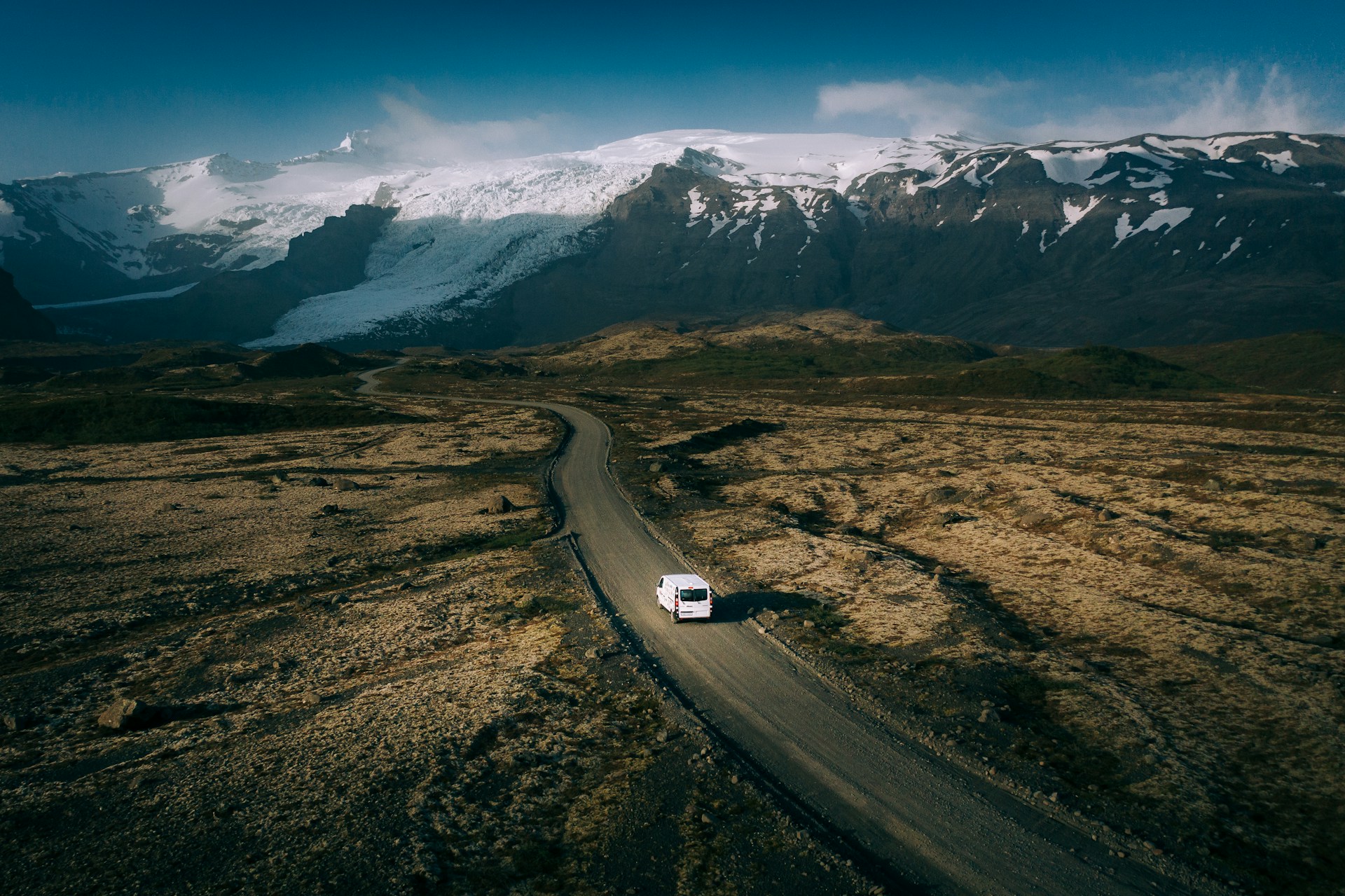 A single van on a gravel road below a glacier